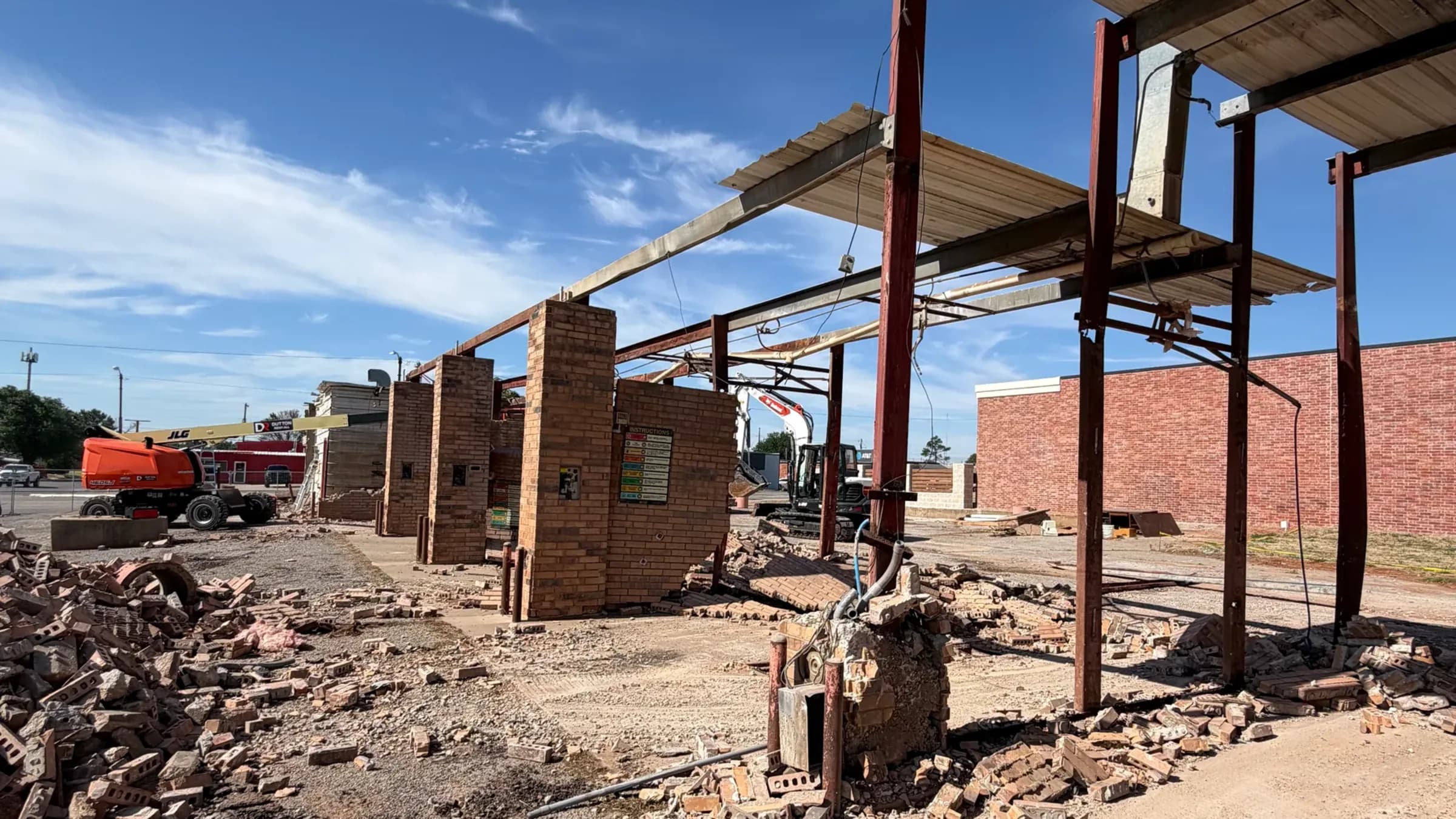 Piles of broken brick where a commercial car wash stood, with the steel canopy frame and one brick column still standing